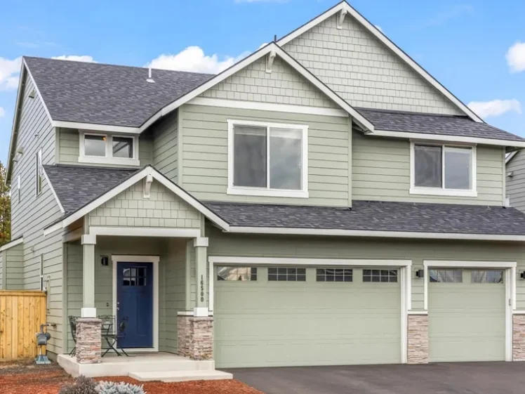 Two-story sage green craftsman home with a navy front door, stone accents and a three-car garage at 16500 Pine Creek Dr, La Pine, OR 97739