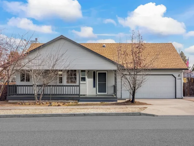 Single-story light grey ranch home with a long front porch and a two-car garage under blue sky at 61388 Elkhorn St, Bend, OR 97702