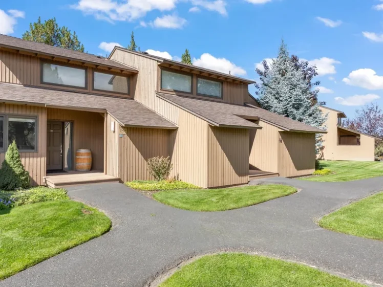 Two-story wood-sided townhome with a covered entry, a front lawn and a paved path at 1965 Redtail Hawk Dr, Redmond, OR 97756